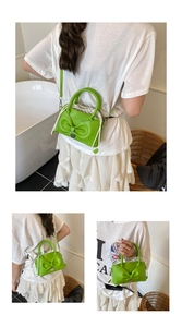 Dettaglio borsa verde con fiocco, ciondolo a cuore e chiusura con coulisse