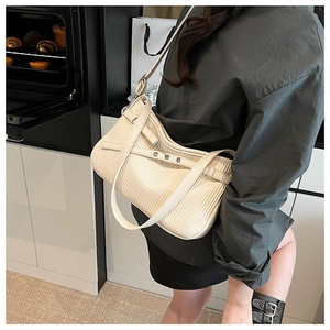Detailed view of cream textured crossbody bucket bag with vertical pleats and metal buckle
