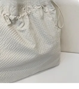 Dettaglio della borsa tote in tela a quadretti crema con tessuto morbido e chiusura a coulisse