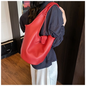 Close-up of red lychee texture leather bucket bag worn on shoulder in a stylish setting