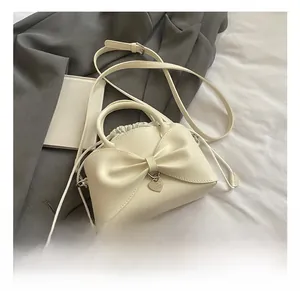 Dettaglio di una borsa a secchiello bianco crema con grande fiocco e ciondolo a cuore
