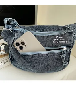 Detail of denim crossbody bag showing front zipper pocket storage for a mobile phone