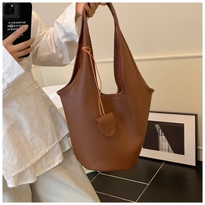 Detail of dark caramel brown leather bucket bag with hanging round flap charm