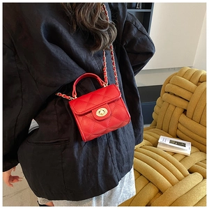 Detail of red quilted leather mini crossbody bag with gold chain strap on yellow sofa