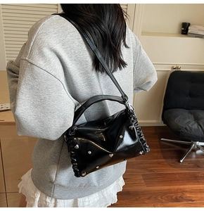 Detailed view of black glossy pillow bag with silver heart studs and pleats