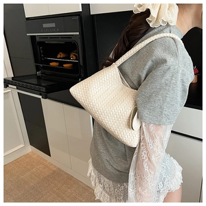 Detail of white woven hobo bag worn by model in a modern indoor kitchen setting