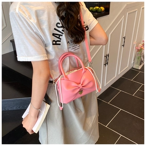 Dettaglio della borsa a secchiello rosa con un grande fiocco e ciondolo a cuore in oro