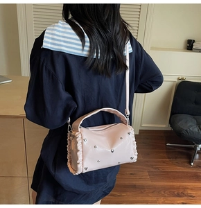 Detail of pink pleated crossbody bag featuring silver heart studs and metallic leather finish