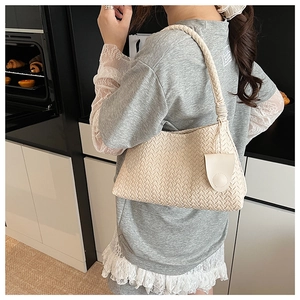 Close-up of cream woven shoulder bag with checkerboard texture and crescent charm