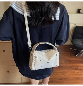 Detailed back view of white pleated crossbody bag with silver heart rivets and ruffles