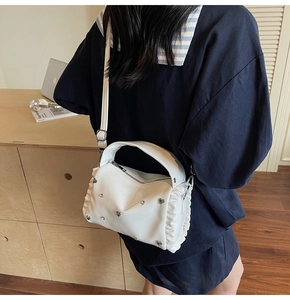 Detail of white pleated shoulder bag with silver heart studs and rhinestone accents