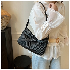 Détail du sac bandoulière noir plissé avec œillets argentés porté par un mannequin en blanc