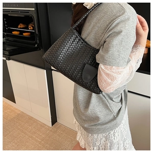 Detail of black leather woven shoulder bag showing intricate Intrecciato texture on person