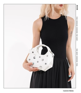Close-up of white studded handbag with metallic rivets and a bow charm detail