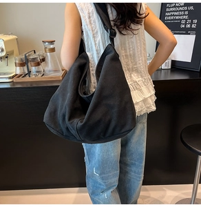 Vista detallada del bolso tote de lona negra usado por una modelo en una cafetería