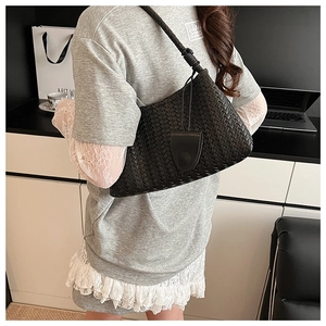 Detail of hand-woven black leather shoulder bag showing thick texture and knotted strap