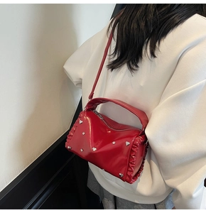 Detail of red patent leather tote with heart studs and pleated sides on a shoulder strap