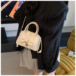 Détail d'un sac seau blanc crème avec nœud décoratif et pendentif cœur argenté