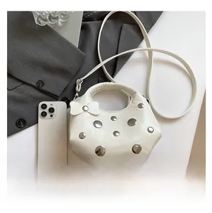 Detail of white leather shoulder bag with silver rivets and bow accent on office desk