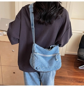 Detail of adjustable denim crossbody bag with metal zippers shown on a model