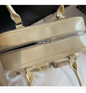 Close-up of cream shoulder bag with silver zipper, lace bow and pearl chain detail