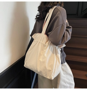 Dettaglio della borsa tote a scacchi crema con chiusura a coulisse indossata da una modella