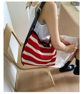 Detail of red and white striped knit tote bag with black leather shoulder strap and buckle