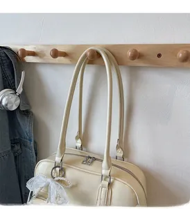 Detail of cream oversized bowling bag with double zipper and lace pearl charm on wooden hanger
