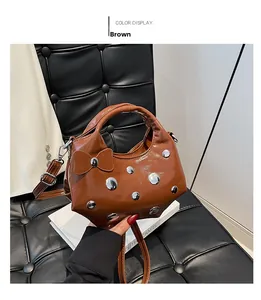 Brown glossy shoulder bag featuring silver rivets and side bow detail on a black sofa
