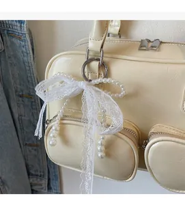 Detailed close-up of a lace bow and pearl charm attached to a cream leather shoulder bag