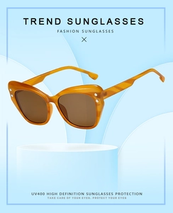 Detailed close-up of amber cat-eye sunglasses with UV400 lenses on white display stand