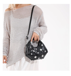 Detail of black rivet handbag with bow charm shown on model in a minimalist style