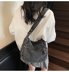 Dettaglio di una borsa a tracolla in denim nero lavato con fibbie argentate indossata da modella