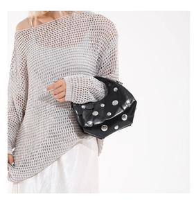 Détail d'un sac à main noir brillant clouté porté par un mannequin en pull gris chic