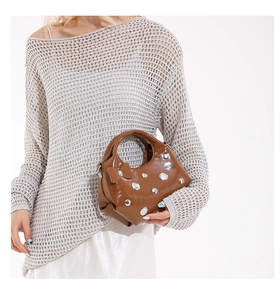 Close-up of brown glossy handbag with silver rivets and matching bow detail