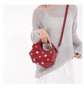 Detail of red patent leather bucket bag with 3D bow and silver rivets worn by a model