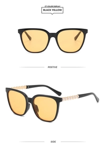 Detail of square sunglasses with black frames, yellow lenses, and pearl-studded temples