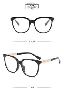 Detail of square black glasses with gold temple arms and faux pearl inlay decorations