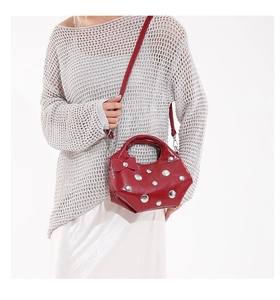 Detail of red strawberry-shaped handbag with silver rivets and leather bow decoration