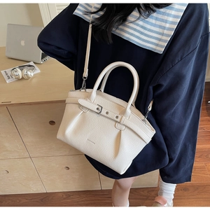 Detail view of cream-colored pebble leather texture and metallic buckle on handbag