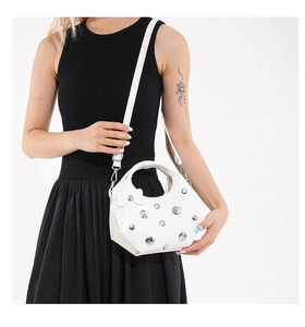 Detail of white studded crescent bag with bow accent and silver metal rivets on white PU leather