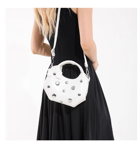 Detailed close-up of a white crescent bag with silver studs and a delicate leather bow