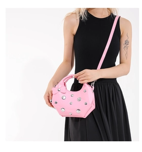 Close-up of pink glossy underarm bag with silver studs and decorative bow detail