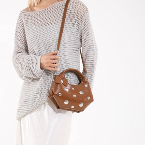 Brown glossy leather underarm bag with silver rivets and bow detail, worn by a model