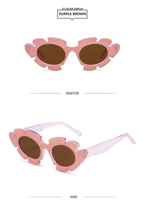 Detailansicht der lila glitzernden Sonnenbrille in Blumenform mit braunen Gläsern für Damen