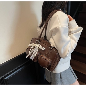 Detail of dark brown glossy shoulder bag featuring lace bows and pearl charms