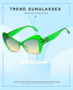 Close-up of green cat eye sunglasses with gradient lenses and gold floral temple detail