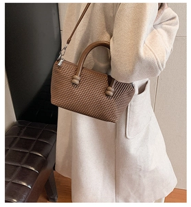 Détail d'un sac marron tressé avec poignée sphérique décorative et ferrures argentées