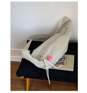 Detail of a creamy nylon dumpling bag with heart charm and woven strap on a bench