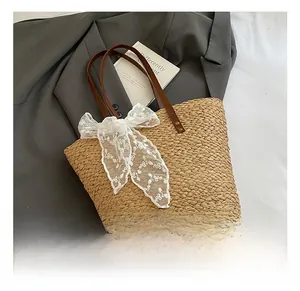 Detail der Stroh-Strandtasche mit weißer Spitzenschleife und braunen Ledergriffen